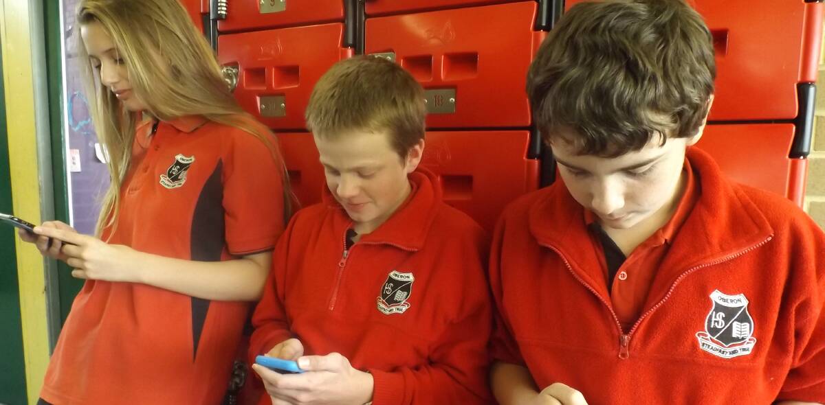SCREEN TIME: Ashleigh Hopson, Grant Perry and Connor Vavasour check out the school’s Facebook page during recess.