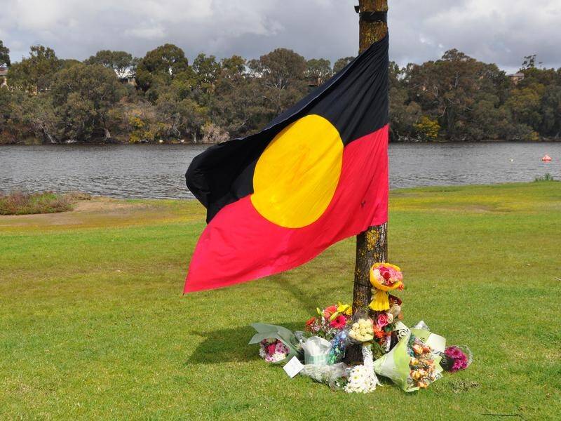 An Aboriginal flag is draped and floral tributes near the scene where two Aboriginal boys drowned.